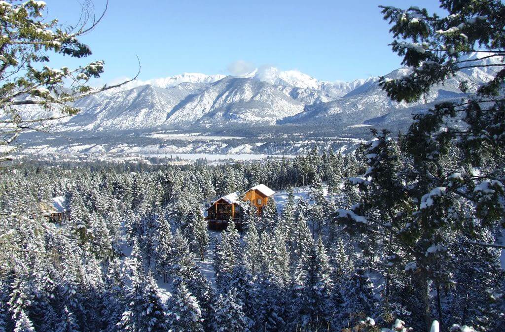 Image of snow-covered valley with beautiful timber framed home and mountains.