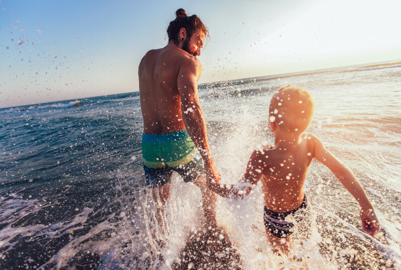 Father and son running through water on a beach