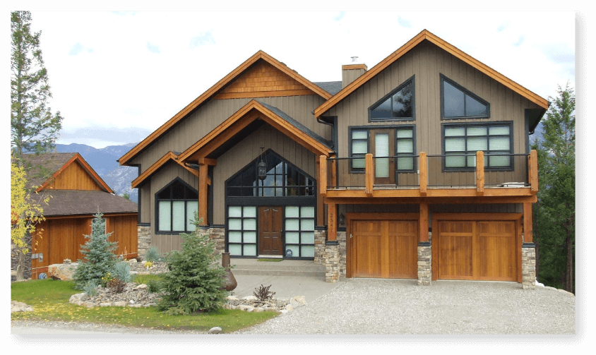 An alpine styled house with two garage doors, landscaped front yard, and a large deck